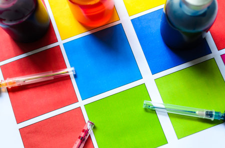 Bottle of ink printer has three colors. Colors is red, yellow and blue with syringe on colored paper.の写真素材