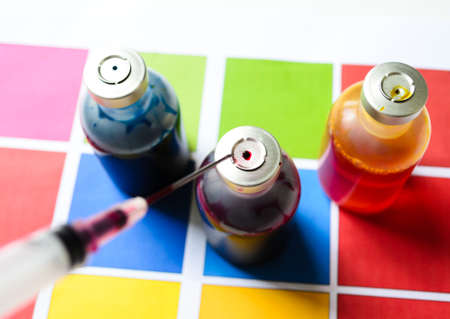 Bottle of ink printer has three colors. Colors is red, yellow and blue with syringe on colored paper.の写真素材