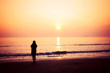 silhouette of woman alone and wave on the beach with sunset in the seaの写真素材