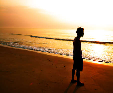 silhouette of man alone and wave on the beach with sunset in the seaの写真素材