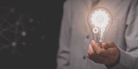A business man's hand holds a light bulb and has a gear iconの写真素材