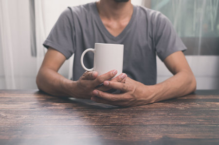 Man holding a glass of water, a coffee mug, on a desk, in his office.の写真素材
