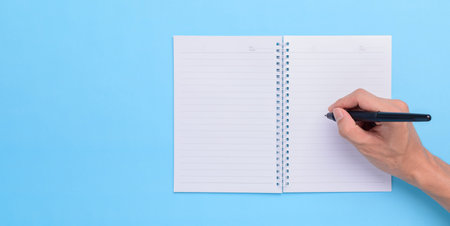 Hand holding a pen to write on a notebook on a blue background
