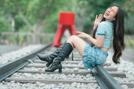 A stylish young woman radiates joy while sitting on train tracks, embodying a carefree spirit in a...