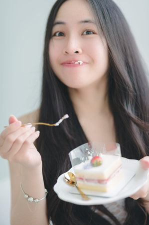 A joyful woman indulges in a delicious slice of cake, savoring each bite. Her playful expression...