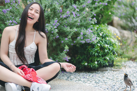 A joyful young woman sits in a lush garden, laughing and enjoying the beauty of nature. Surrounded by vibrant flowers and greenery, her happiness is contagious.の写真素材