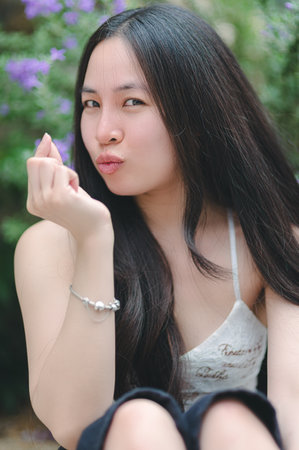 A young woman enjoys the outdoors, posing playfully with long hair and a charming smile. Surrounded by flowers, she exudes a joyful and stylish vibe.の写真素材