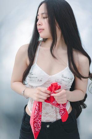 A stunning portrait of a woman wearing a delicate lace top and holding a red bandana, displaying elegance and confidence in a serene indoor setting.の写真素材