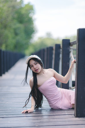 A young woman in a pink dress poses gracefully on a wooden walkway surrounded by nature, capturing a serene moment filled with beauty and elegance.の写真素材