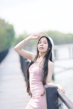 A young woman wearing a pink dress and a hat poses confidently on a boardwalk beside a tranquil lake, capturing the essence of summer beauty and serenity.の写真素材