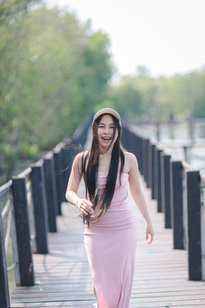 A cheerful woman walks along a wooden pathway, surrounded by lush greenery. Her joyful expression and flowing hair capture the essence of carefree moments in nature.の写真素材