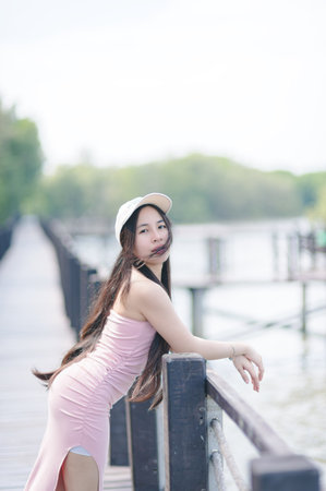 A serene portrait of a young woman posing elegantly on a dock by the water, exuding beauty and confidence amidst nature's tranquil backdrop.の写真素材