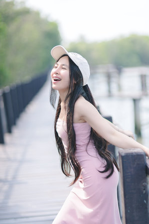A joyful young woman laughs and enjoys a sunny day on a scenic boardwalk. Her carefree spirit is captured in this vibrant outdoor setting, surrounded by nature.の写真素材
