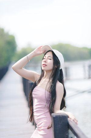 A young woman in a pastel dress poses confidently on a sunlit pathway, enjoying the gentle breeze and vibrant surroundings. Her playful spirit shines through as she embraces nature.の写真素材