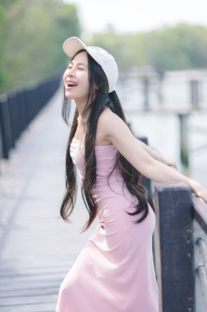 A joyful young woman laughs heartily on a scenic boardwalk, surrounded by nature. Her sunny demeanor and casual style create a vibrant and serene atmosphere.の写真素材