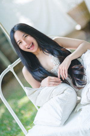 A joyful woman with long hair beams with happiness while lounging on a sunlit outdoor bed. The natural setting enhances her carefree spirit and beauty.の写真素材