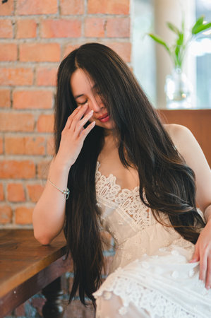 A young woman with long flowing hair poses gracefully in an elegant dress, radiating calm and beauty against a rustic brick wall backdrop.の写真素材