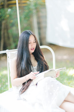 A young woman with long hair enjoys reading a magazine while lounging in a sunlit outdoor setting. The serene atmosphere creates a perfect moment of relaxation and beauty.の写真素材