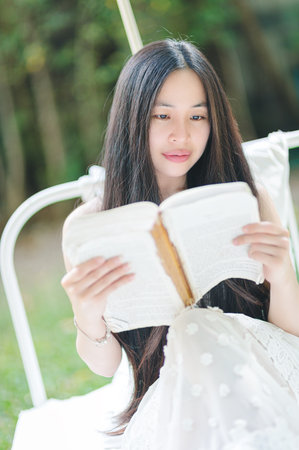 A young woman enjoys reading a book in a peaceful outdoor garden, surrounded by nature. Her long hair cascades as she immerses herself in literature, capturing a moment of serenity and joy.の写真素材