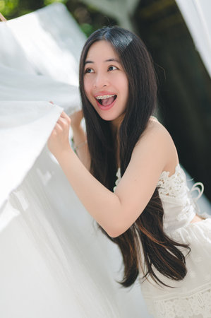 A cheerful woman with long hair poses outdoors, holding flowing fabric with joy. Her radiant smile and playful spirit capture the essence of happiness in a bright, natural setting.の写真素材