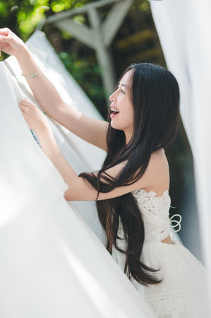 A joyful woman interacts with white curtains, embracing the sunlight in a bright indoor setting. Her smile radiates happiness and elegance.の写真素材