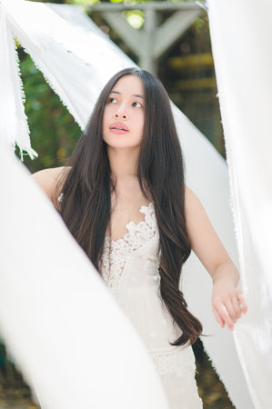 A graceful woman with long hair stands among flowing white fabric in a serene outdoor setting, radiating beauty and tranquil emotion in natural light.の写真素材