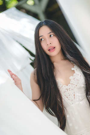 A serene portrait of a woman with long hair captured in sunlight, showcasing elegance and beauty while posing in flowing white fabric against a natural backdrop.の写真素材
