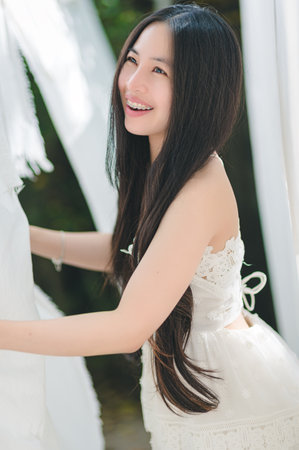 A young woman enjoys a moment outdoors, smiling beautifully in a flowing white dress. Her long hair complements the serene atmosphere, radiating joy and beauty.の写真素材