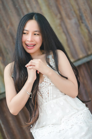 A joyful young woman with long hair stands against a rustic background, exuding happiness and charm. Her playful demeanor captures the essence of youth and beauty.の写真素材