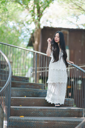 A graceful woman in a beautiful dress walks down a staircase surrounded by lush greenery, embodying elegance and serenity in a peaceful outdoor setting.の写真素材