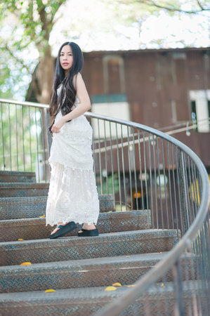 A fashionable young woman stands gracefully on a decorative staircase, showcasing her elegance. The natural light highlights her stylish attire amidst a serene outdoor backdrop.の写真素材