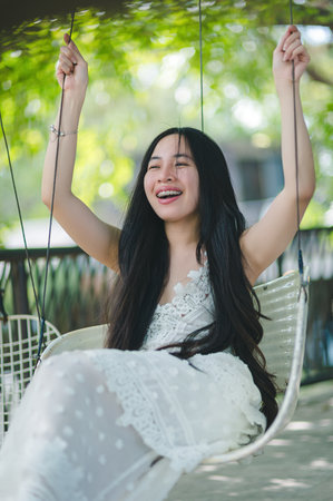 A joyful young woman swings blissfully outdoors, surrounded by vibrant greenery. Her laughter and carefree spirit radiate in the warm sunlight, capturing pure happiness.の写真素材