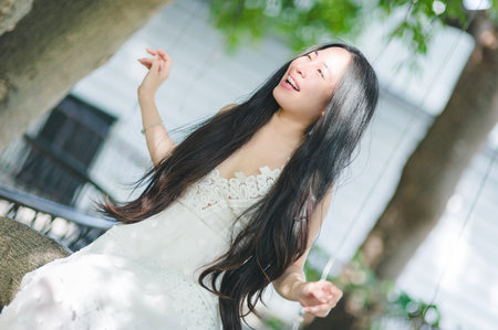 A joyful woman in a flowing dress dances in a sunlit natural setting, surrounded by greenery. Her long hair cascades as she expresses pure happiness and serenity.の写真素材