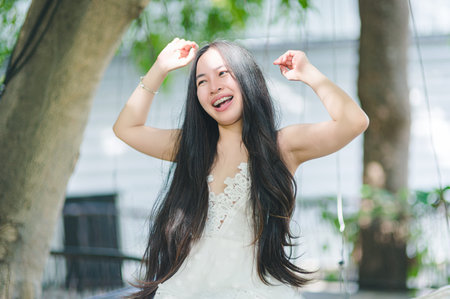 A joyful woman swings in a lush outdoor setting, her long hair flowing freely as she smiles brightly. The scene captures a carefree moment filled with joy and happiness.の写真素材