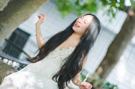A joyful young woman with long hair experiences the beauty of nature, surrounded by greenery and basking in the warm summer sunlight, embodying freedom and happiness.の写真素材