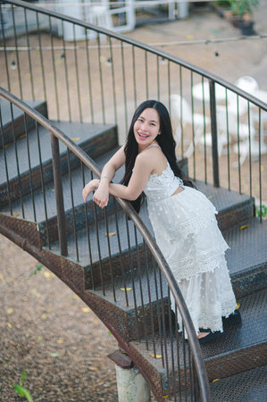 A joyful woman wears a white dress and poses gracefully on a spiral staircase in an outdoor setting, capturing a moment of happiness and elegance.の写真素材