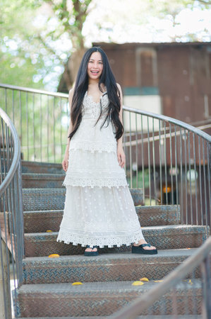 A joyful woman stands on a spiral staircase wearing an elegant white dress. The natural setting and soft sunlight create a serene and cheerful atmosphere.の写真素材