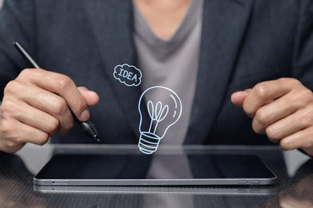 A person holds a pen above a tablet, illustrating an idea with a light bulb sketch. This image captures creativity and innovation in a modern workspace setting.の写真素材