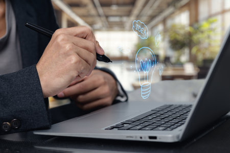 A professional individual brainstorming creative ideas using a pen and laptop in a modern office. Visual elements represent innovation and inspiration for projects.の写真素材