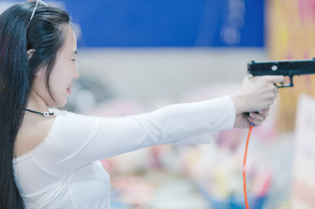 A young woman confidently aims a handgun in a colorful indoor setting, showcasing focus and determination. This image captures the thrill of recreational shooting and the empowerment of female engagement in traditional male-dominated activities.の写真素材