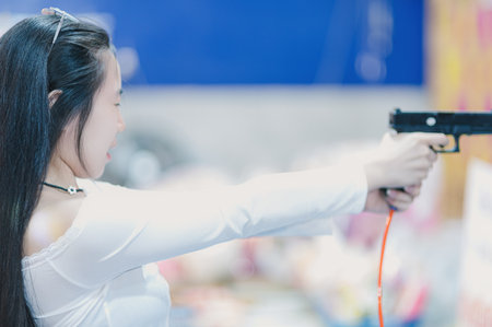 A young woman focuses as she aims a toy gun in a colorful indoor environment. This playful scene captures joy, innocence, and creativity.の写真素材