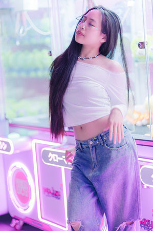 A confident young woman poses playfully in a whimsical urban setting, showcasing casual fashion against a backdrop of vibrant neon lights and a cheerful atmosphere.の写真素材