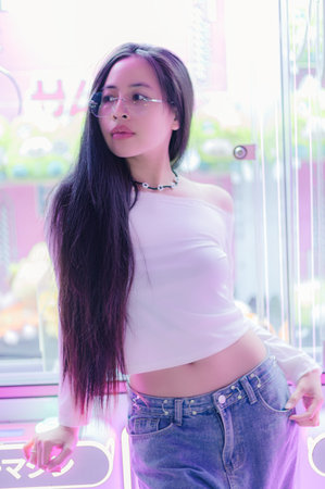 Fashionable woman with long hair poses confidently in a vibrant urban setting. Surrounded by neon lights, she showcases a stylish and contemporary look.の写真素材