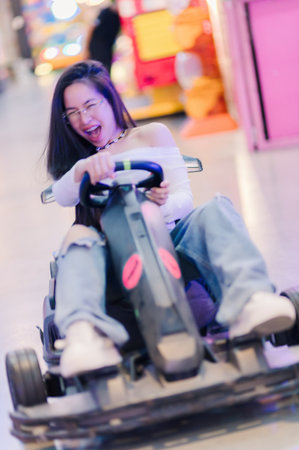 A young woman rides a go-kart with enthusiasm, embodying joy and excitement in a lively amusement environment filled with colorful lights and playful energy.の写真素材