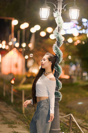 A young woman poses gracefully near illuminated street lamps, surrounded by festive lights. The serene atmosphere captures a blend of joy and style in an urban setting.の写真素材