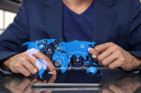 A businessman interacts with a digital tablet displaying a world map and various global icons, emphasizing technology and connectivity in the modern business environment.の写真素材