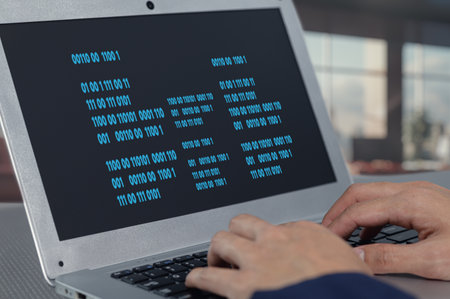 A close-up view of hands typing code on a laptop, showcasing a binary screen. This image reflects technology, programming, and the modern digital workspace.の写真素材