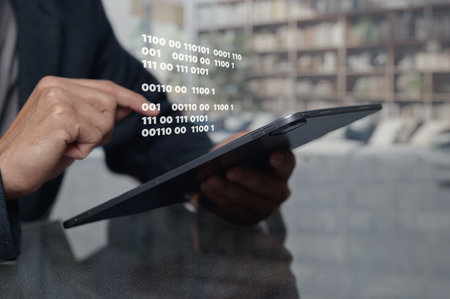 A man uses a tablet showing binary code in a sleek office space, emphasizing the fusion of technology and data processing in modern business environments.の写真素材