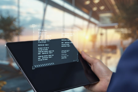 A person holds a tablet displaying a digital coding interface in a modern workspace with bright sunlight, showcasing the intersection of technology and design.の写真素材