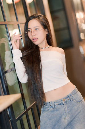 A stylish young woman with long hair poses confidently indoors, wearing a casual outfit consisting of a cropped top and denim skirt. The atmosphere is relaxed and inviting.の写真素材
